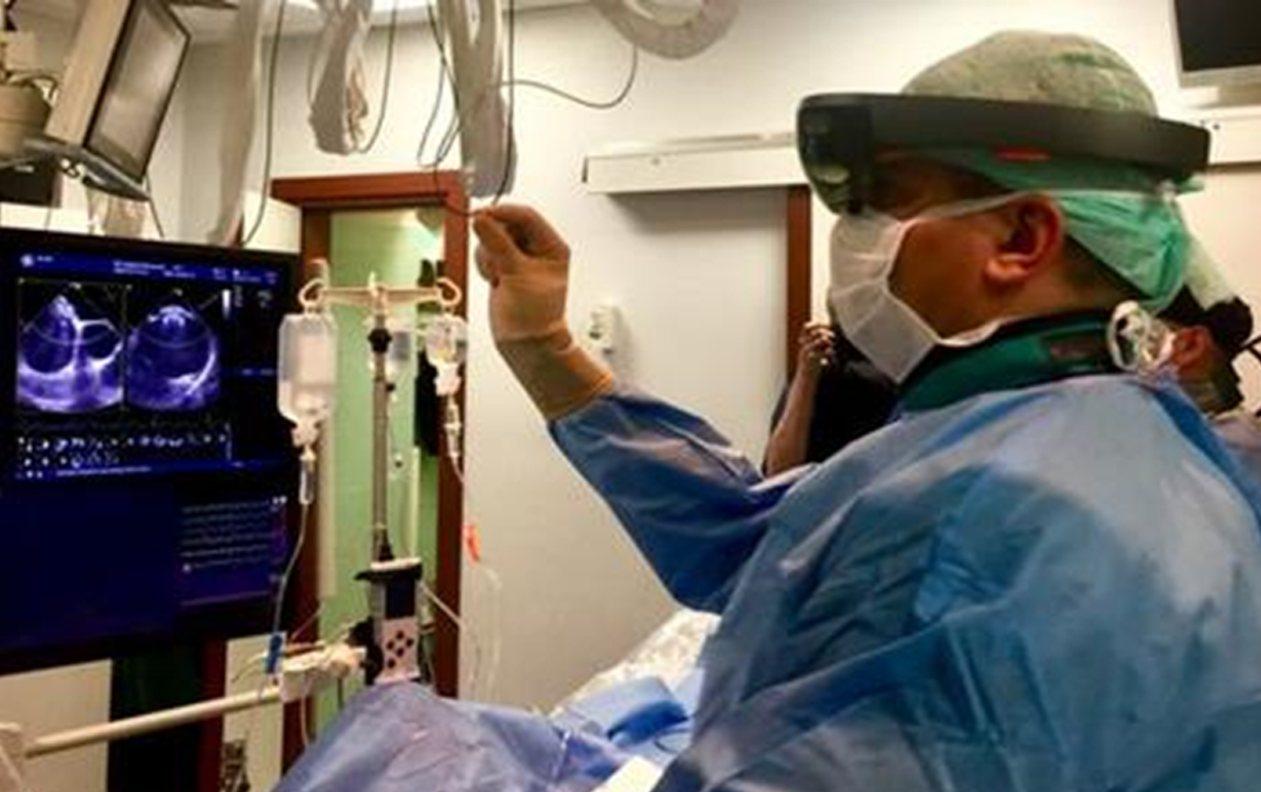 Clinician wearing a HoloLens headset beside an echocardiography monitor in a cath lab